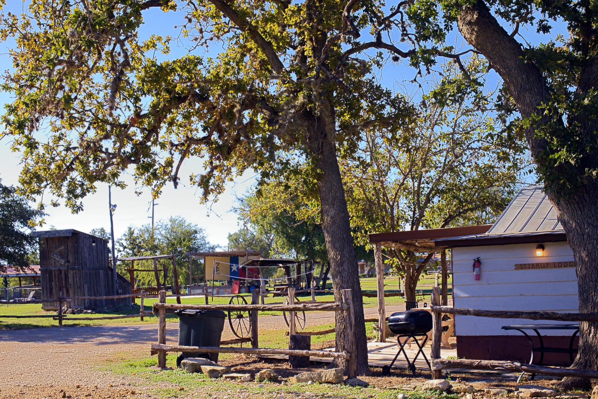 Cabins under big live oaks, with a cedar rail fence, a grill and a picnic table out front