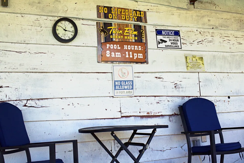 The porch by the pool: a clock, a Twin Elm pool-hours sign and two blue chairs against a weathered white wall