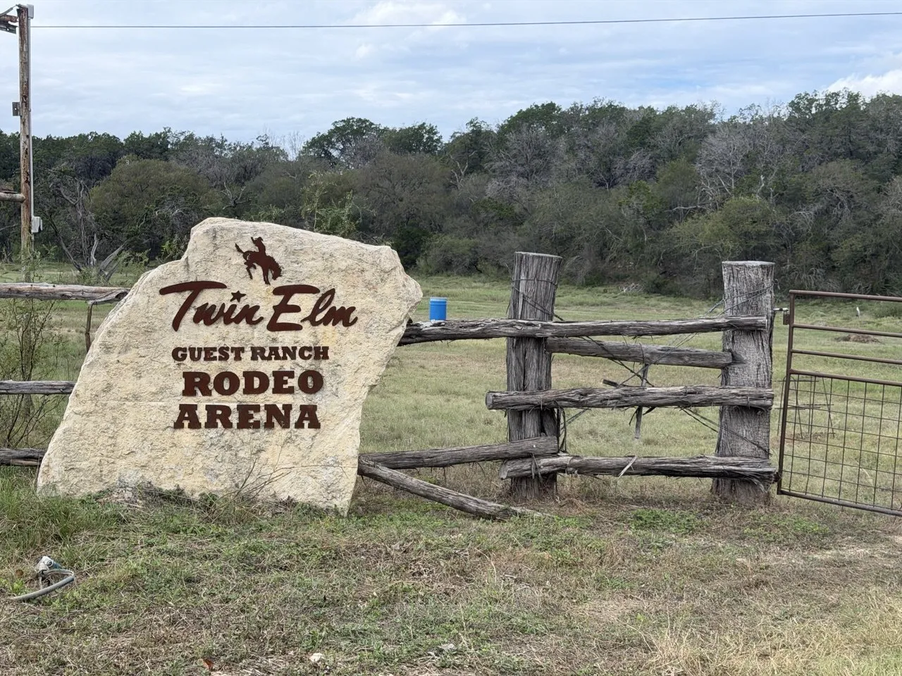 The limestone Twin Elm Guest Ranch Rodeo Arena sign beside a cedar-post fence