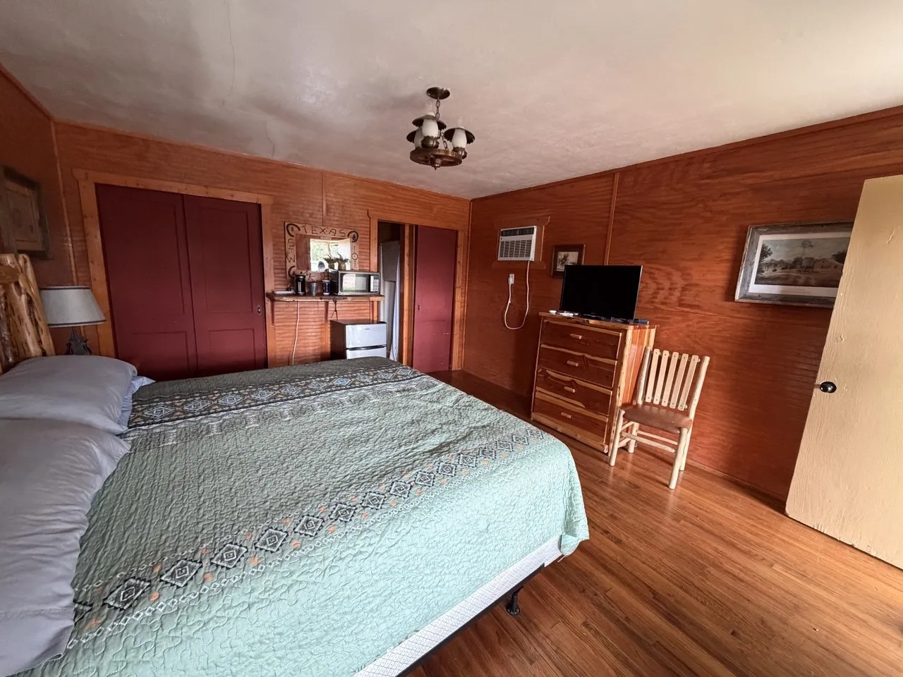 A cabin interior with a king bed, wood-paneled walls, a dresser with a TV and a coffee corner