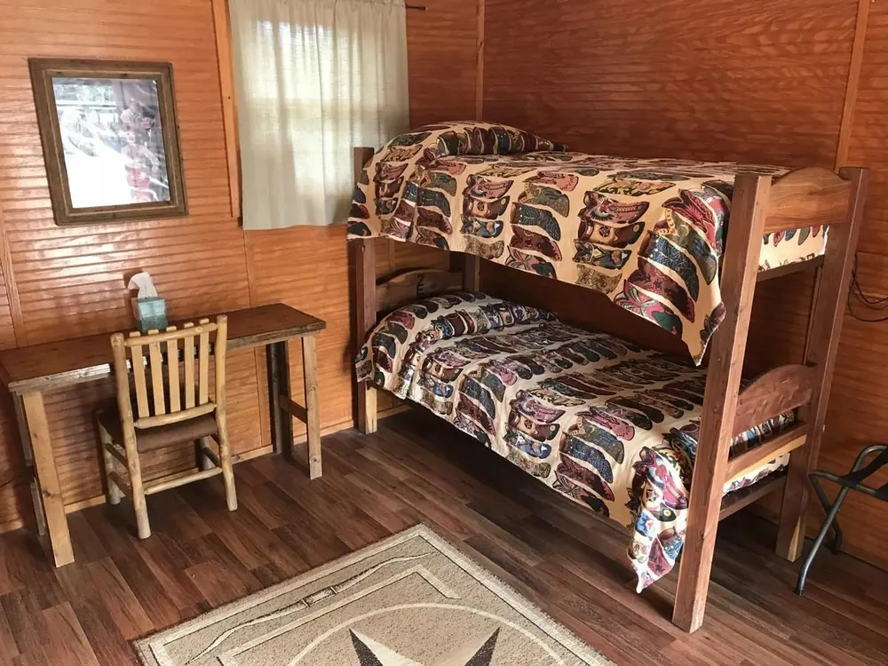 A Bunkhouse room with a wooden bunk bed in boot-print quilts, a writing desk and a star rug