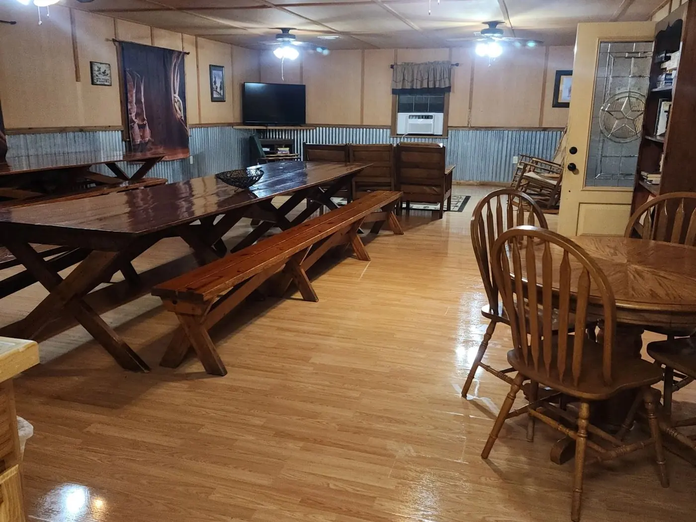 The Clubhouse: long wooden tables with benches, round tables and chairs on a wood floor under ceiling fans