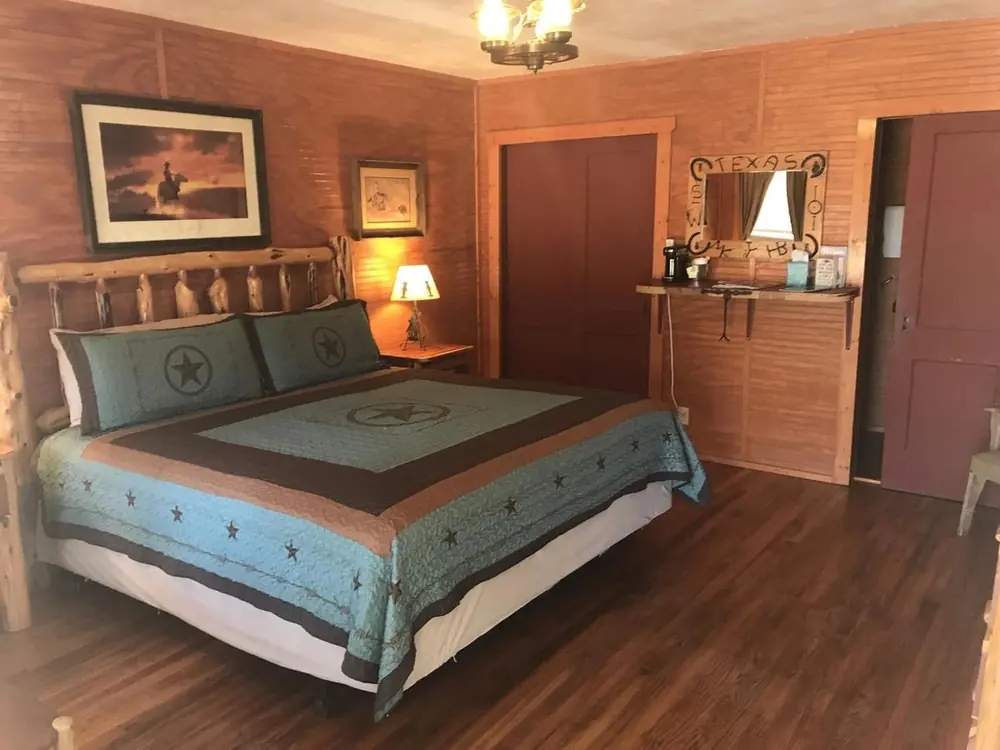 The Honeymoon Corral: a log king bed with a turquoise Texas-star quilt, wood-paneled walls and a coffee shelf