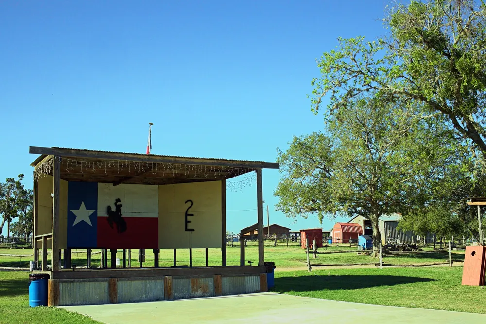 The covered stage painted with the Texas flag, a bronc rider and the 2E brand, on the lawn under big trees