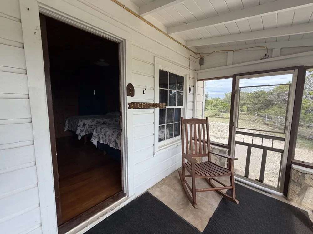 The screened porch outside room 6: a wooden rocker, the Stompeders sign beside the open door and the ranch beyond the screen